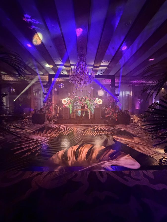 Ballroom stage under a crystal chandelier with purple beams and Air Motion tops either side of the booth