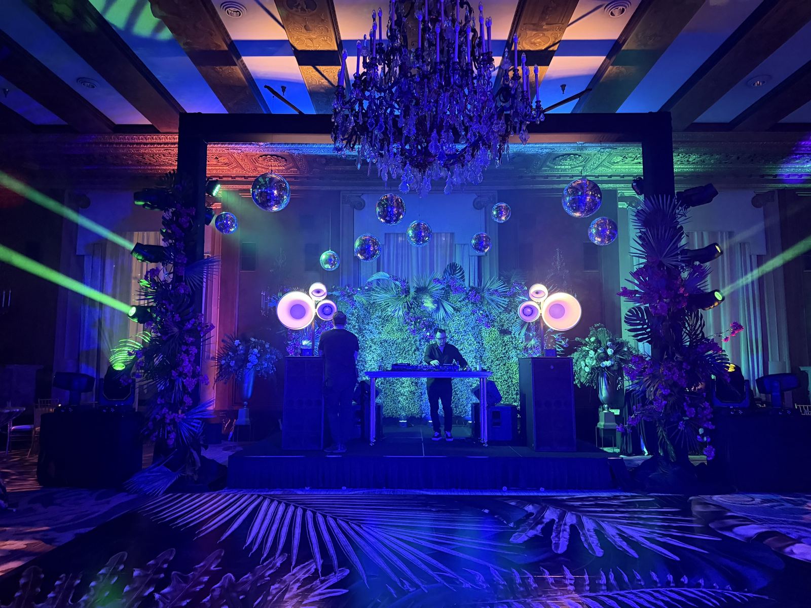 A ballroom stage with Void Air Motion tops on either side of the DJ booth, mirror balls overhead and green beams crossing the room