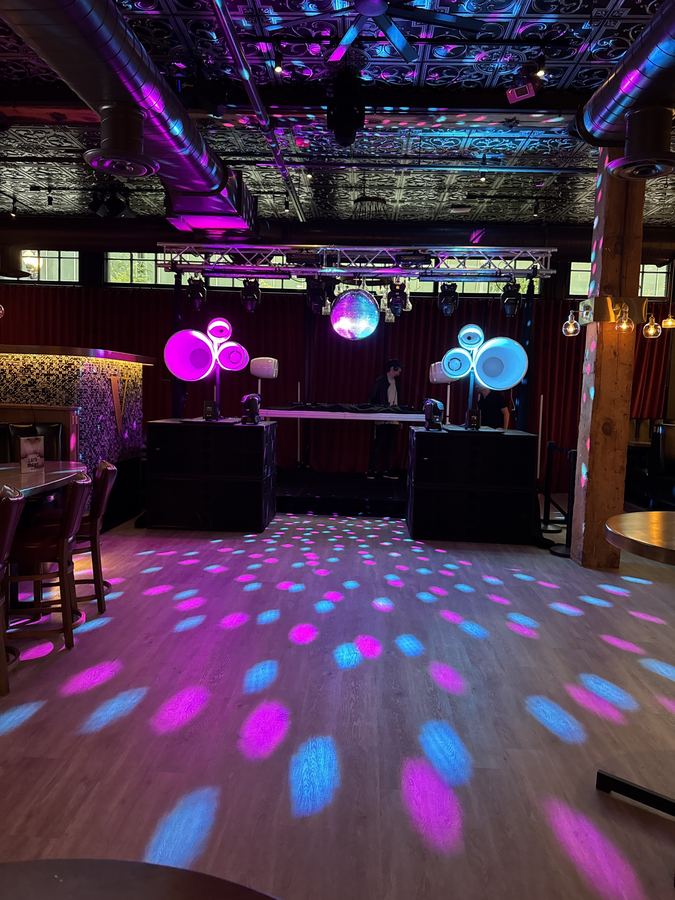 Club room with Air Motion tops lit magenta and cyan on XV2 subs and mirror ball light across the floor