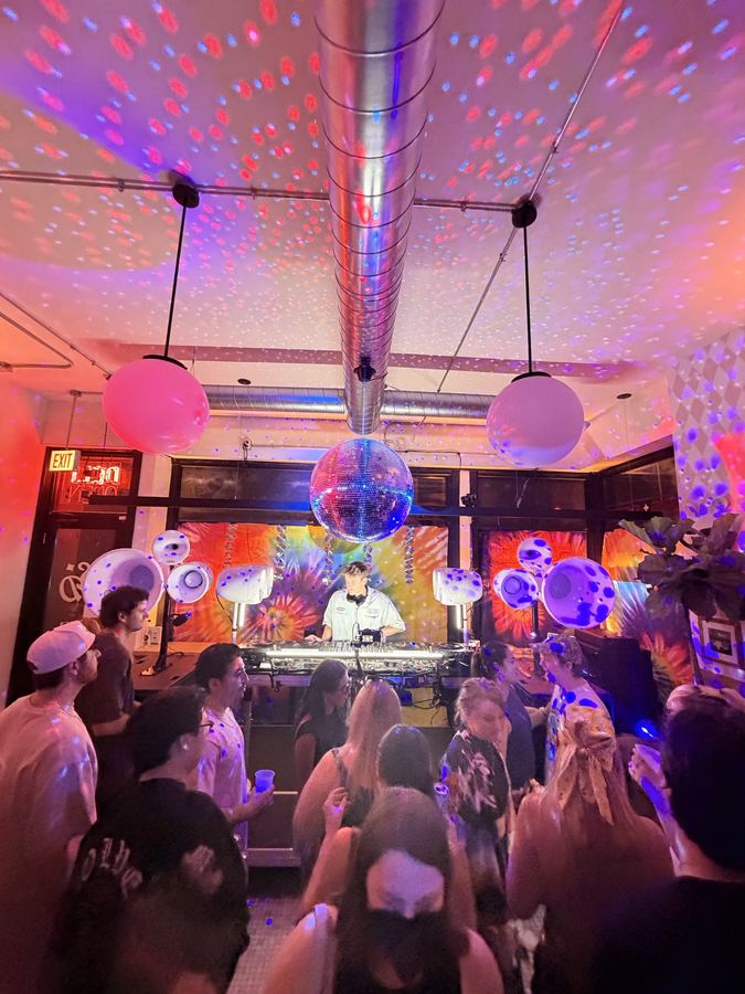 Small room party with a mirror ball, white Void horns flanking the DJ and a tie-dye backdrop