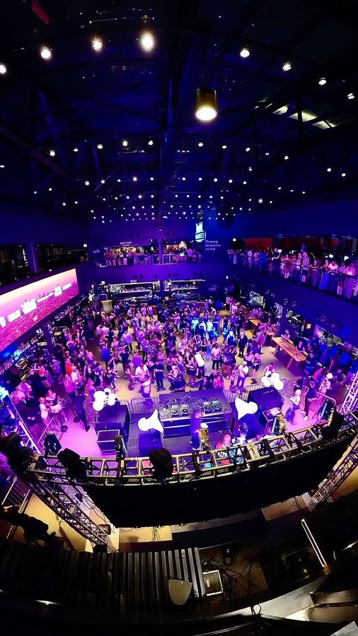 Overhead view of a crowded dance floor in a market hall with the DJ booth and Air Motion tops below