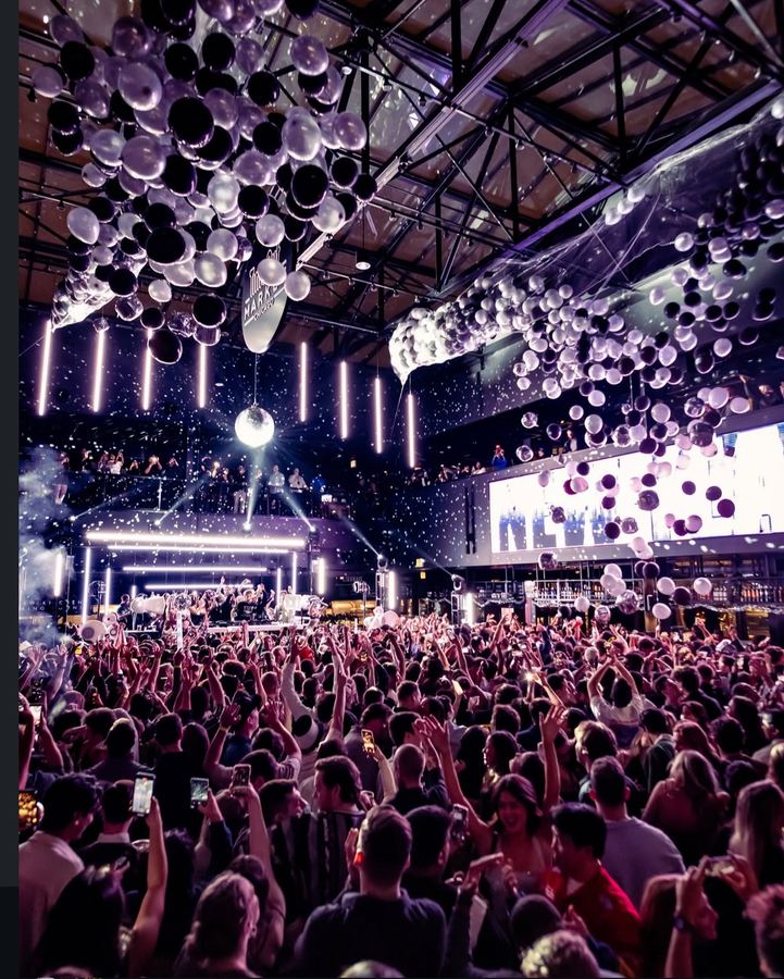 Crowd with hands up under a balloon drop and mirror ball at a New Year’s Eve party