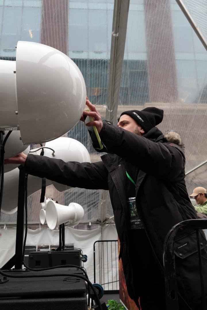 Crew member adjusting a white Air Motion horn on top of the sub stack inside a clear event tent